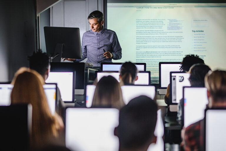 Mid adult professor teaching a lecture from desktop PC at computer lab.
